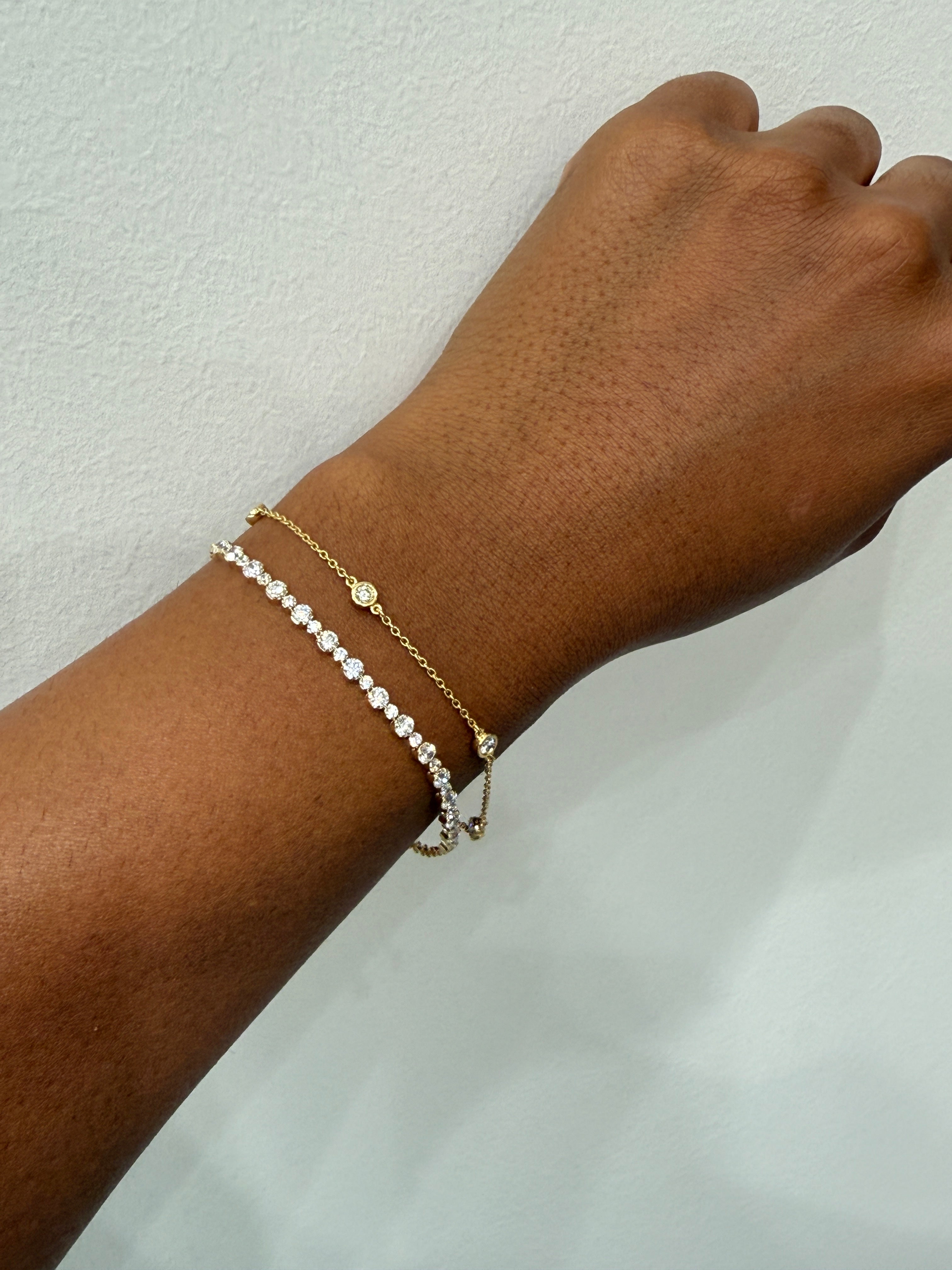 Hand wearing a gold bracelet with a pearl charm on a light background