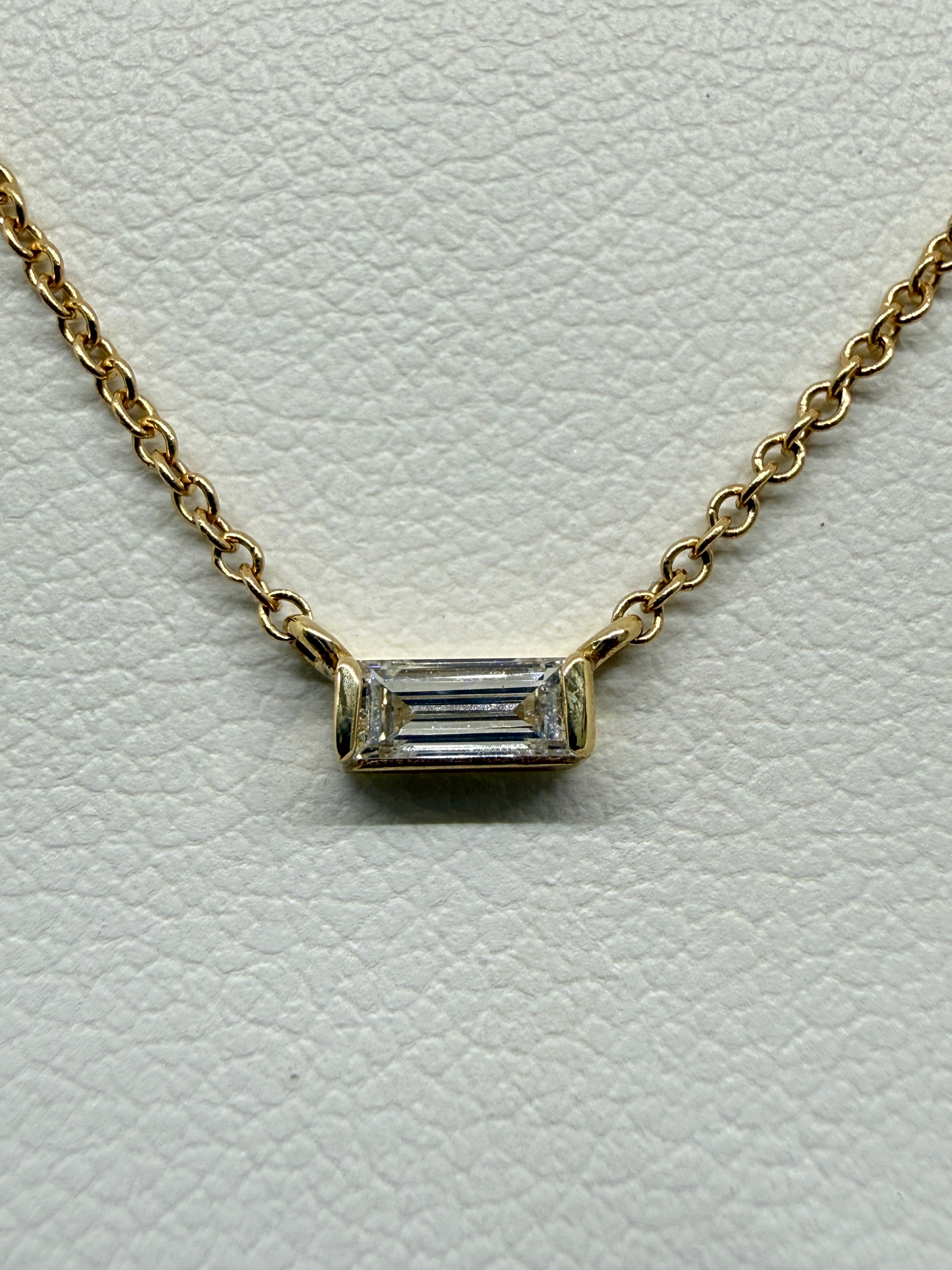 Gold necklace with a rectangular diamond pendant on a light gray background